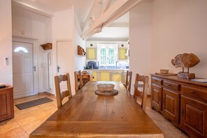 Une salle à manger avec une table et des chaises en bois, une cuisine en arrière-plan et un buffet en bois orné d’une sculpture de poisson.