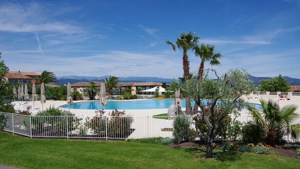 Zona de piscina con palmeras, una valla blanca y cielo azul despejado.