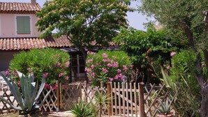 Un jardín con una cerca de madera, un árbol con flores rosadas y un edificio con tejado de tejas.