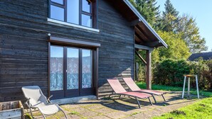 Una casa de madera con un patio, dos sillones y una pequeña mesa.