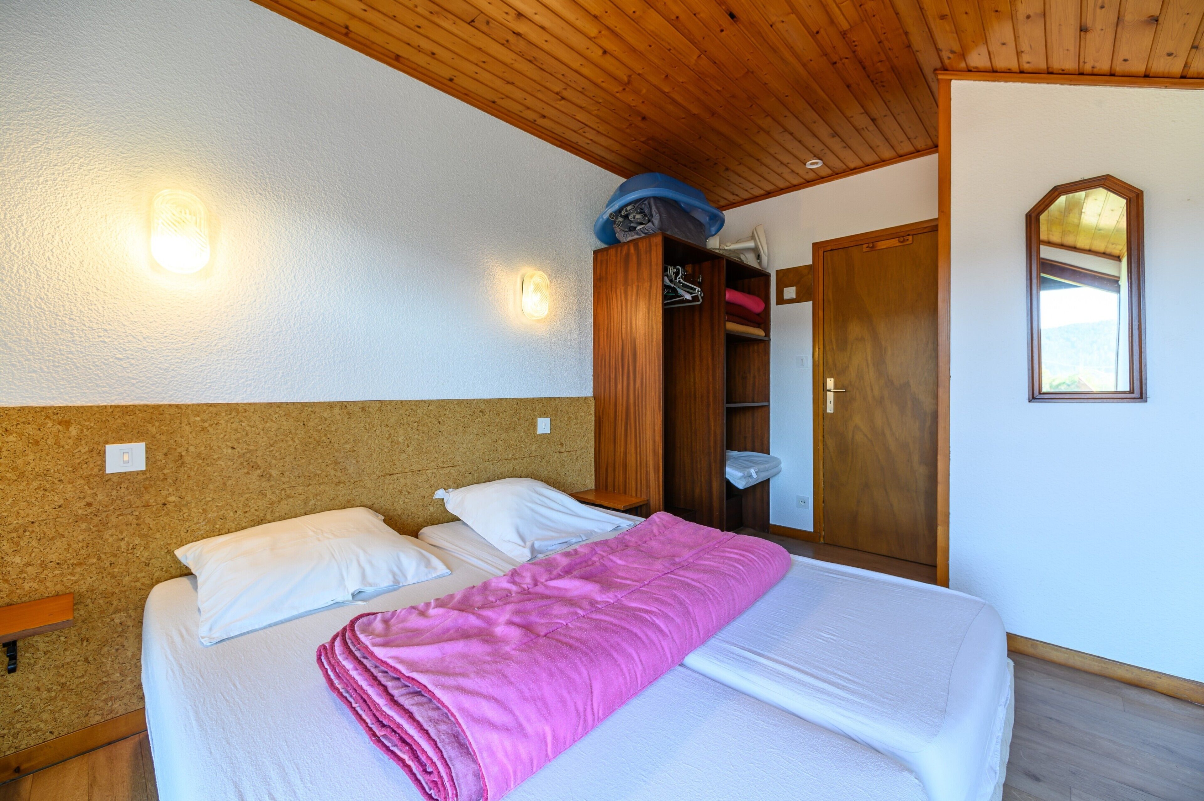 A bedroom with a bed, a wooden wardrobe, and a mirror on the wall.