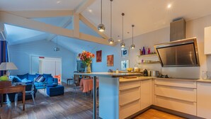 A modern kitchen with a central island, pendant lighting, and a dining area with a blue sofa and table.