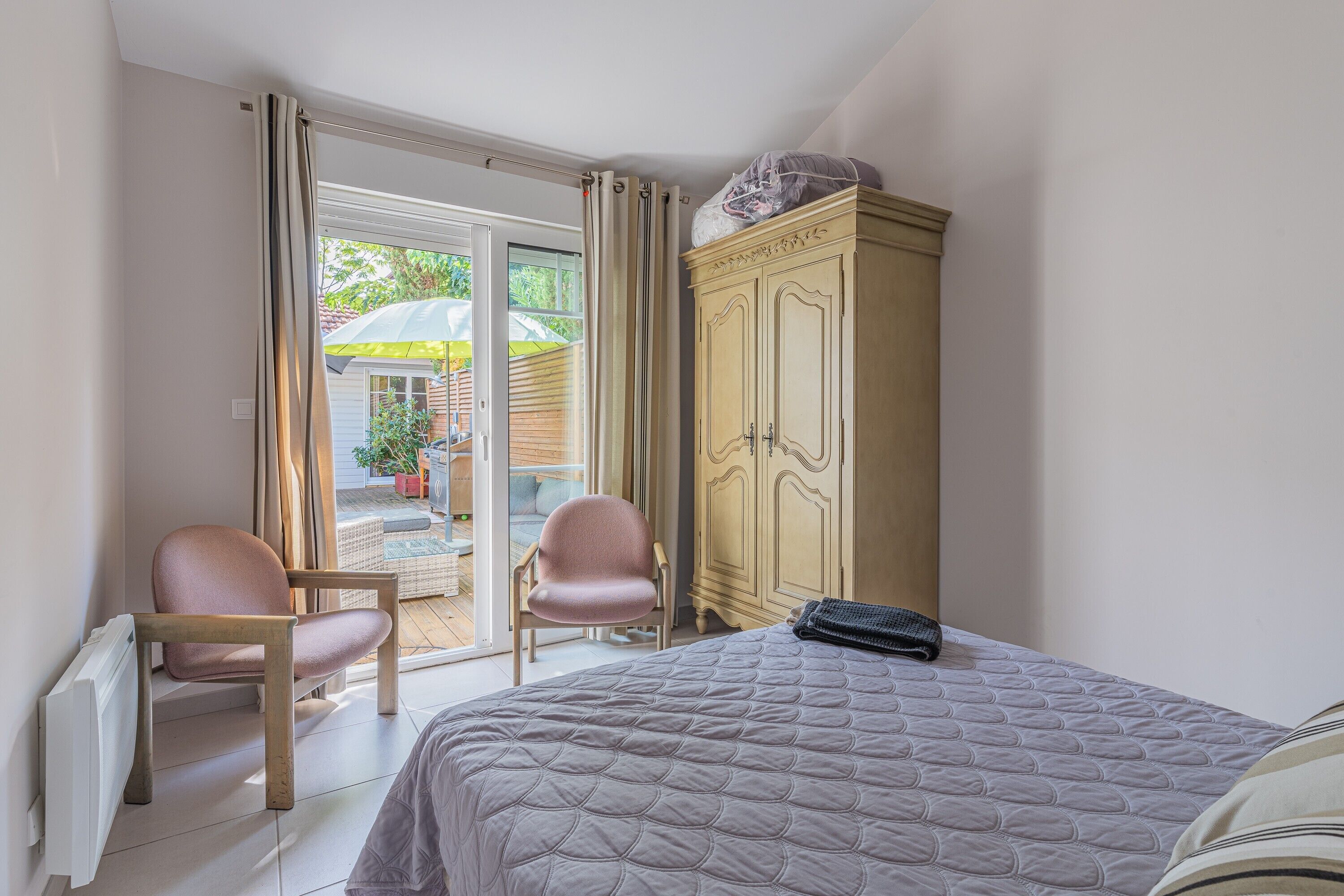 A bedroom with a bed, a wardrobe, a chair, and a sliding glass door leading to an outdoor area.