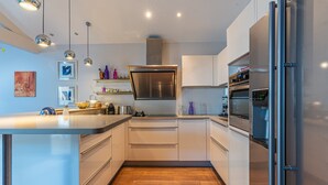 A modern kitchen with white cabinets, stainless steel appliances, and pendant lighting.