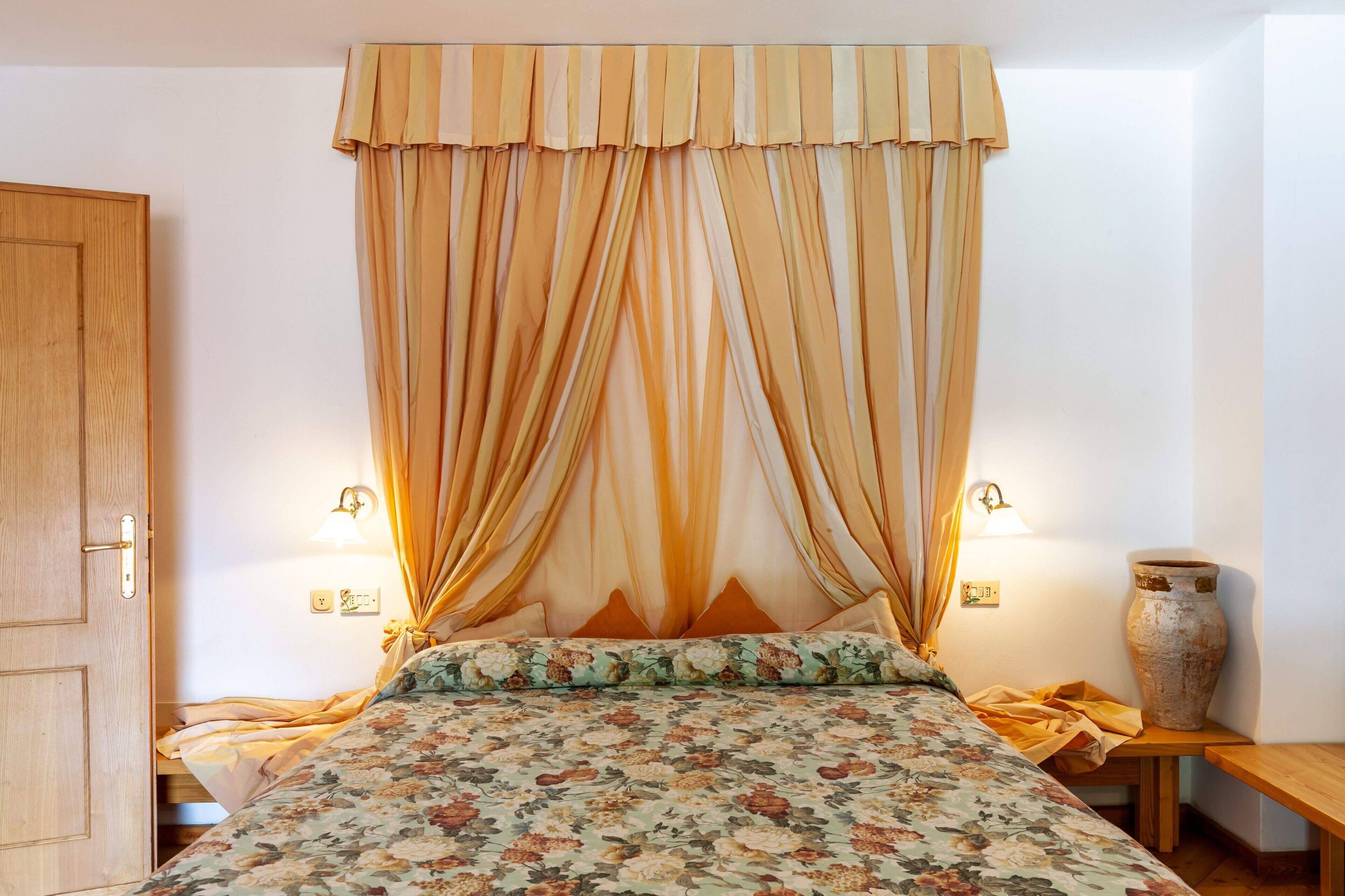 A bedroom with a bed, curtains, a nightstand, a lamp, and a vase.