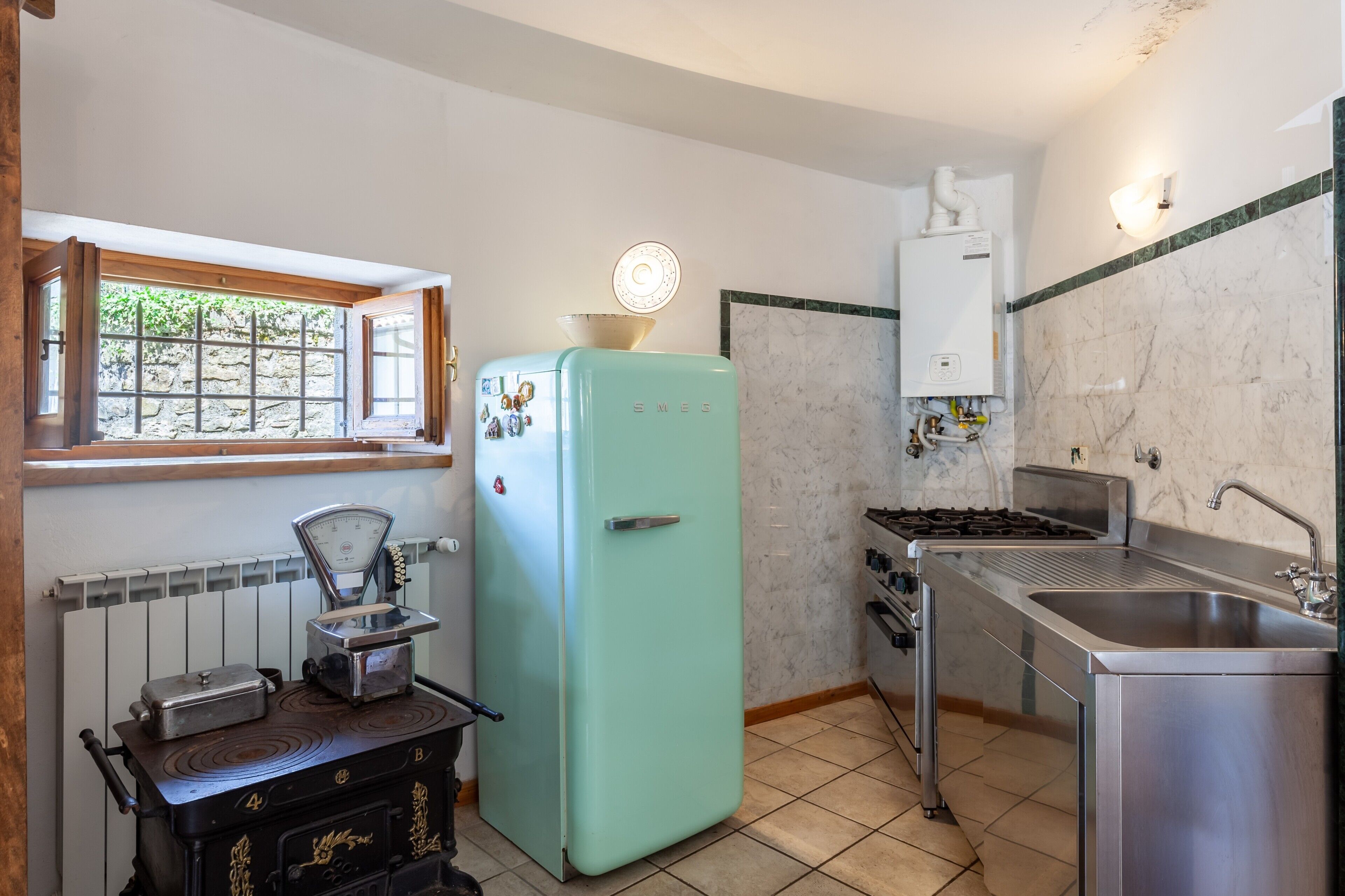 Une cuisine équipée d’un réfrigérateur vintage, d’une cuisinière, d’un évier et d’une fenêtre donnant sur un paysage verdoyant.