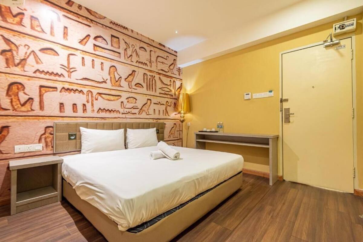 Una habitación de hotel con una cama, una mesita de noche, una pared decorada con jeroglíficos, un escritorio y una puerta.