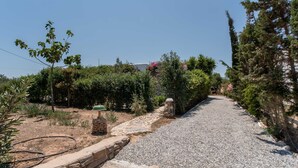 A gravel pathway leading through a garden with stone walls and various plants. - Holiday Home 'Green Retreats 1 Paros' with Mountain View, Wi-Fi and Air Conditioning (Glifades)