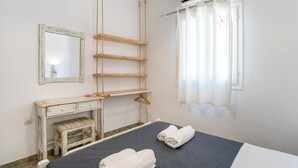 A bedroom with a bed, a desk, a mirror, a hanging rack, and a window with curtains. - Holiday Home 'Green Retreats 1 Paros' with Mountain View, Wi-Fi and Air Conditioning (Glifades)