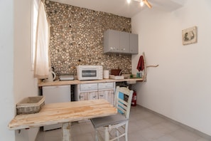 Une cuisine avec un revêtement mural en pierre, un four à micro-ondes, un petit réfrigérateur et une table en bois avec une chaise.