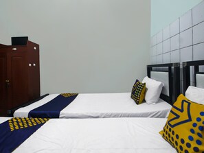 Habitación de hotel con dos camas, cada una con ropa de cama blanca y mantas de colores azul y amarillo. Se observa un armario de madera y un espejo con marco negro en la pared.