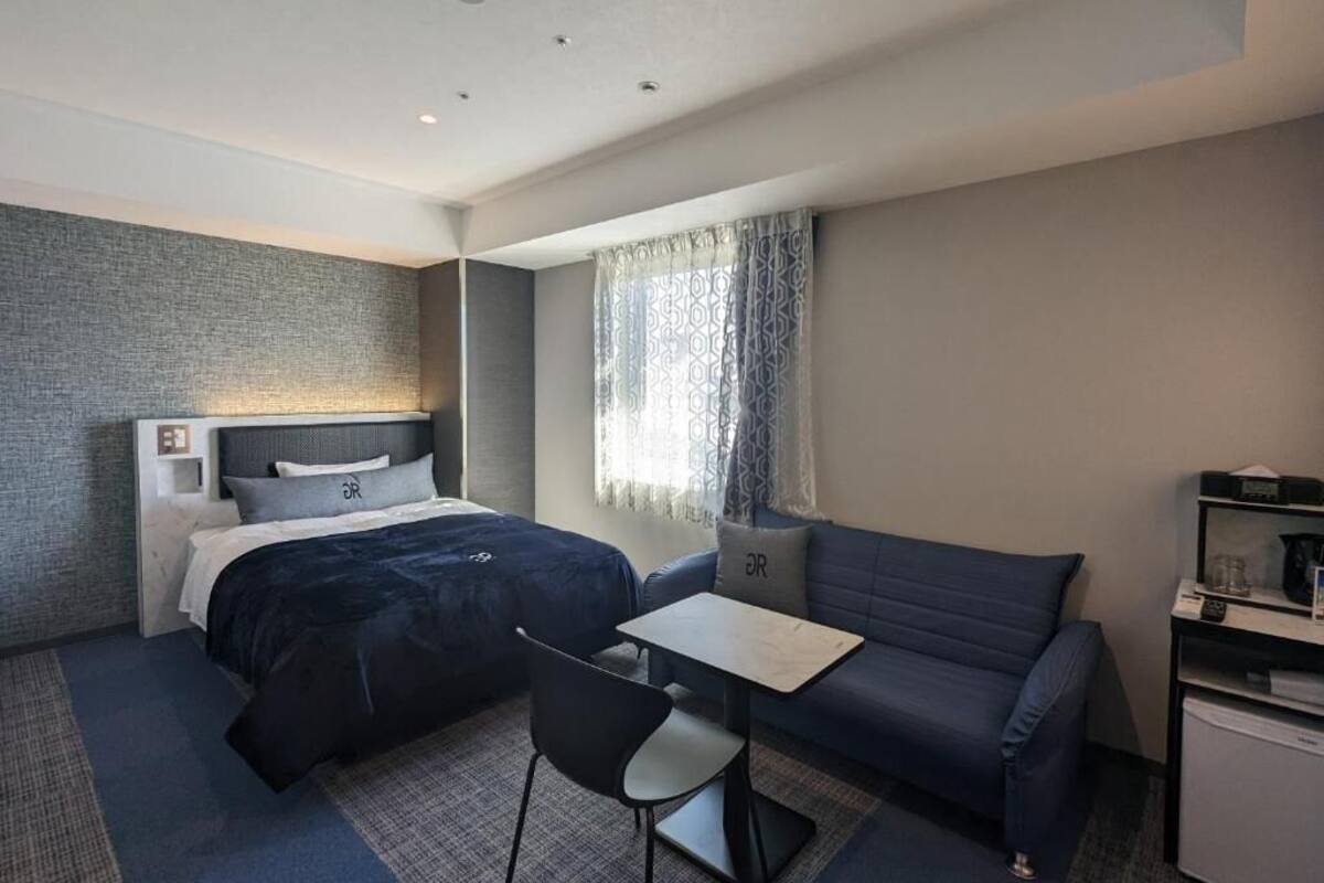 Una habitación de hotel moderna con una cama, un sofá, una mesita y un escritorio con una computadora.