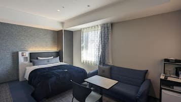 Una habitación de hotel moderna con una cama, un sofá, una mesita y un escritorio con una computadora.