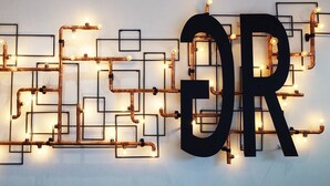 Una pared con una instalación de luces decorativa que incluye tuberías expuestas y bombillas, formando las letras 