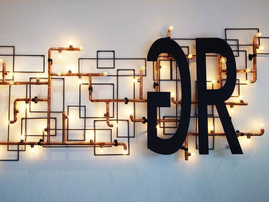 A wall with a decorative light installation featuring exposed pipes and bulbs, forming the letters "OR".