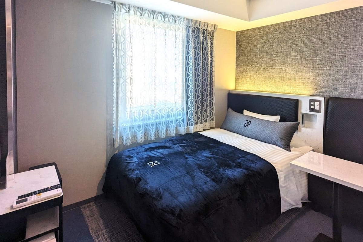 Habitación de hotel moderna con cama, mesita de noche y cabecera con pared texturizada.