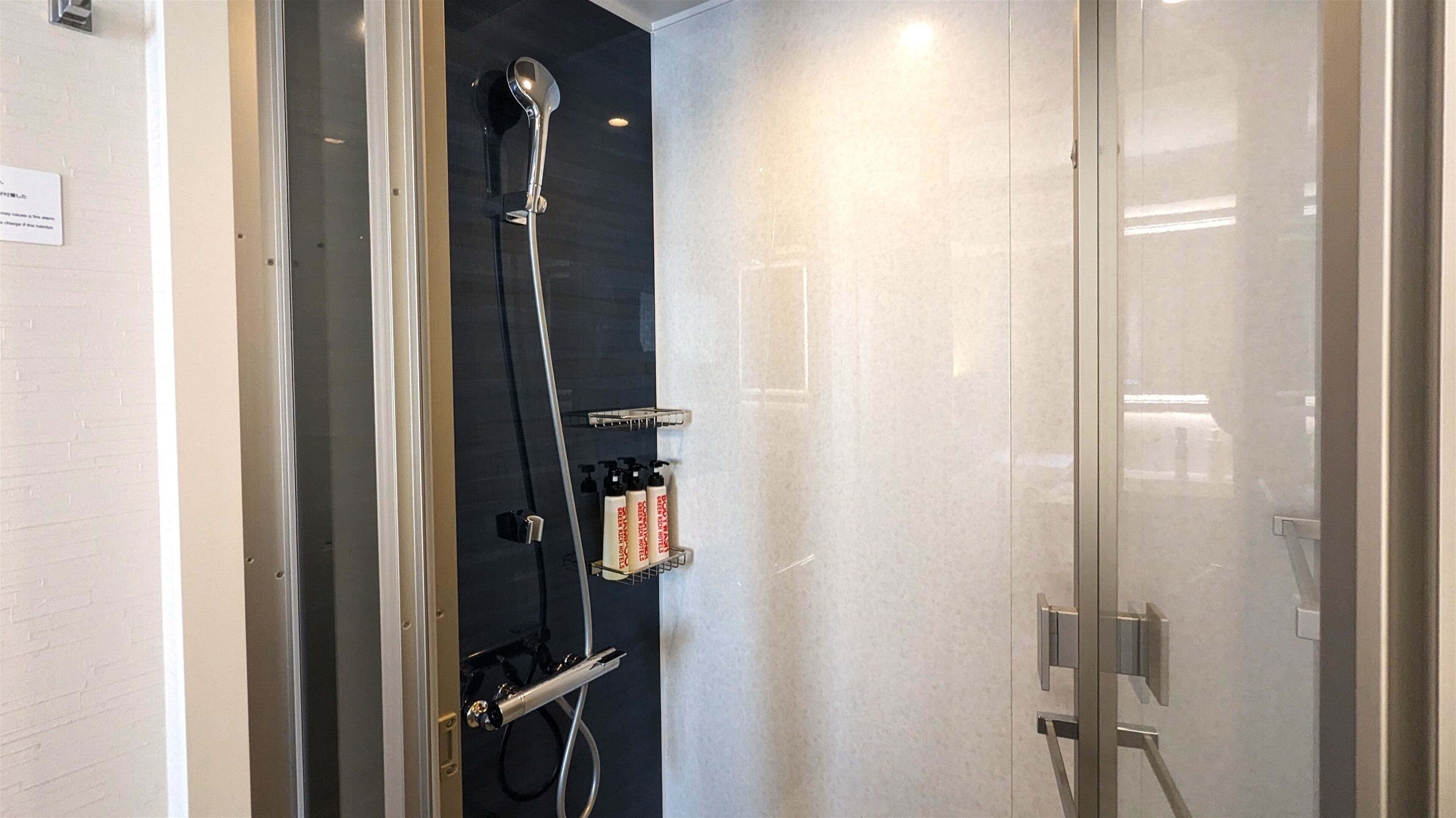 A modern shower with a handheld showerhead, a handheld shower attachment, and a wall-mounted faucet. There are toiletries on a shelf.