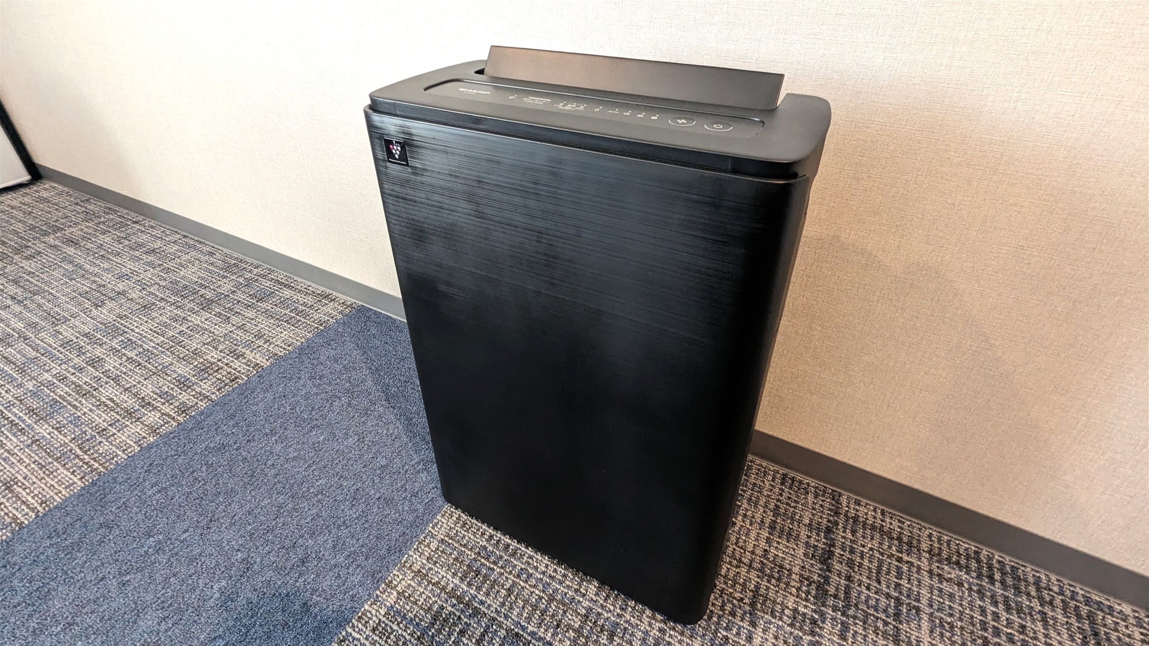 A black printer in a corner of a room with a carpeted floor.