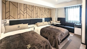 Una habitación de hotel con dos camas, una mesita, un sofá y un ventanal con cortinas.