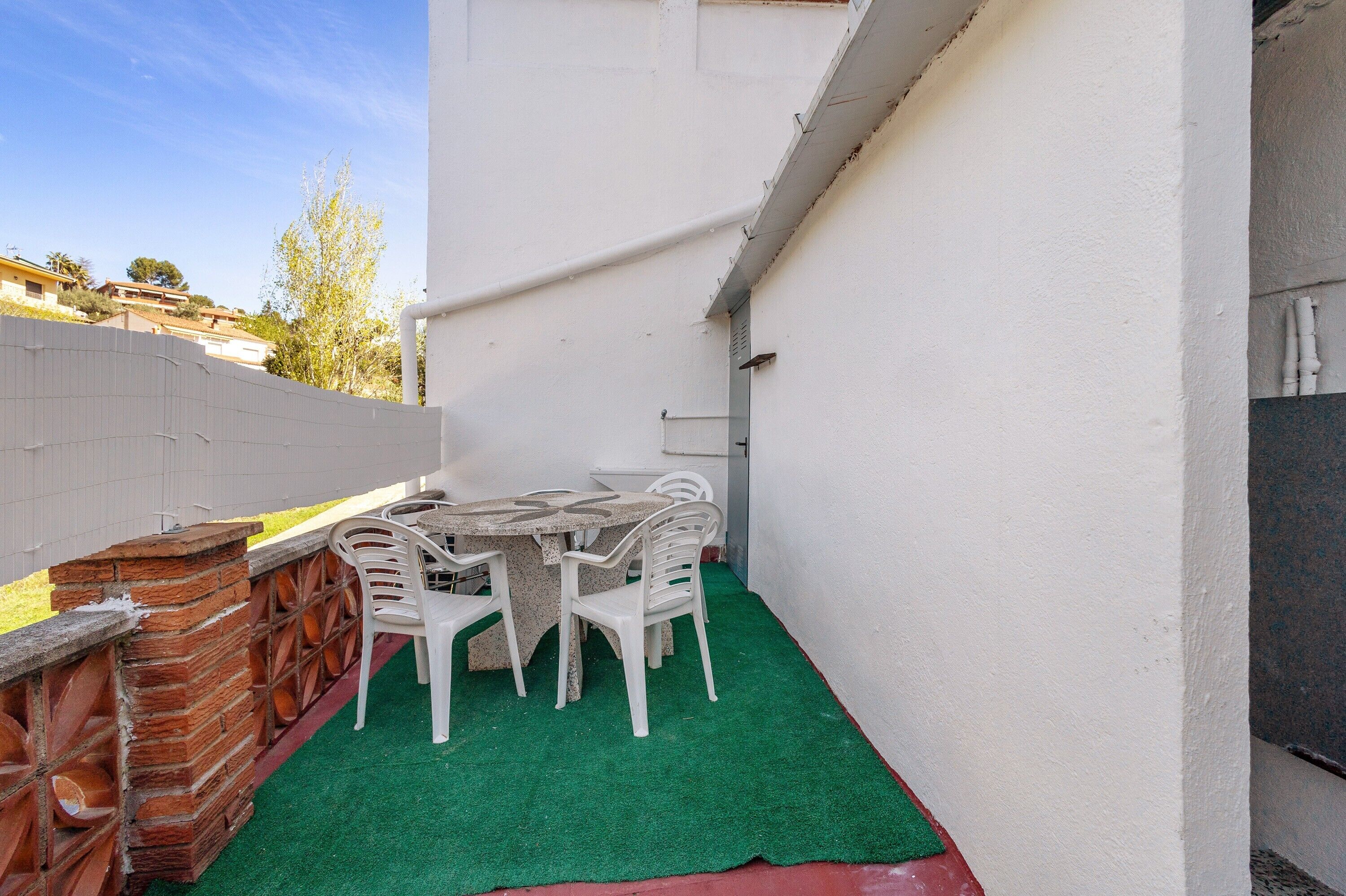 Un pequeño patio al aire libre con una mesa y sillas, un muro de ladrillo y una valla blanca.