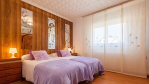A bedroom with two beds, wooden paneling, artwork, and a sliding door closet. - Villa 'Cal Ramon for 15 Guests' with Private Pool, Wi-Fi & Air Conditioning (Rubi , Barcelona)