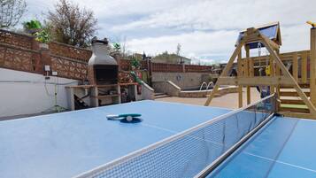 A ping pong table with a net, a wooden swing set, and a brick oven in a backyard.