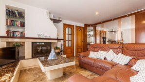 A living room with a brown leather sofa, a coffee table, a fireplace, and a bookshelf. - Villa 'Cal Ramon for 15 Guests' with Private Pool, Wi-Fi & Air Conditioning (Rubi , Barcelona)