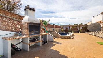 Un patio exterior con horno de ladrillo, piscina, sillas de descanso y una pérgola.