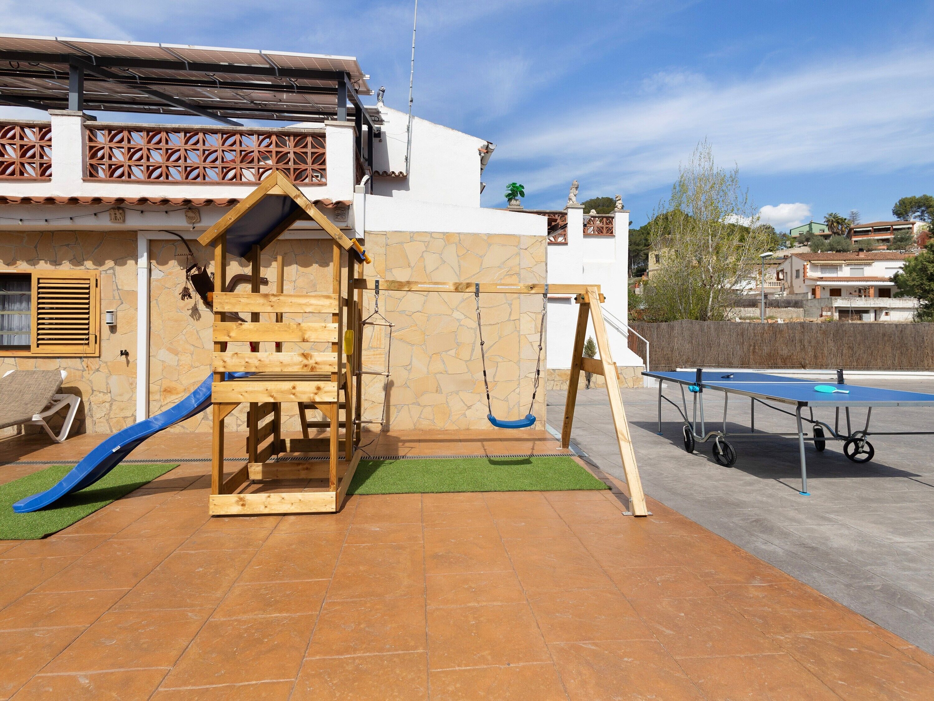 Un área de juegos infantiles con un columpio de madera, un tobogán y una mesa de ping pong.