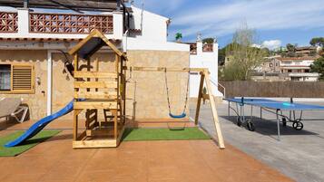 Un área de juegos infantiles con un columpio de madera, un tobogán y una mesa de ping pong.