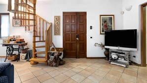 Una sala de estar con una escalera de madera, un televisor plano grande, una puerta de madera y una máquina de coser.