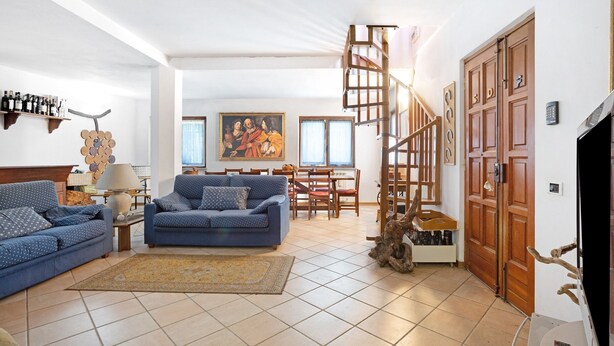 Una sala de estar con un sofá azul, una mesa de centro, una lámpara, un cuadro, una escalera y una puerta de madera.