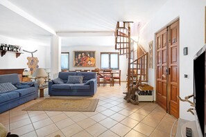 A living room with a blue sofa, a coffee table, a lamp, a painting, a staircase, and a wooden door. - Apartment 'La Torre' with Mountain View, Private Terrace and Wi-Fi (Arcola)