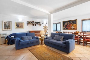 A living room with two blue sofas, a coffee table, a rug, a fireplace, and a dining area with wooden chairs and a table.