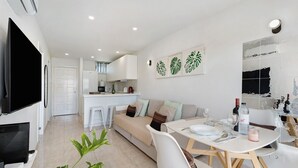 Ein modernes Wohnzimmer mit Sofa, Esstisch und Fernseher.
