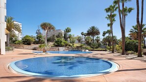 Ein Swimmingpool mit Steinrand, umgeben von Palmen und einem Gebäude im Hintergrund.