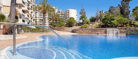 A swimming pool with a curved edge, surrounded by a stone wall and palm trees.