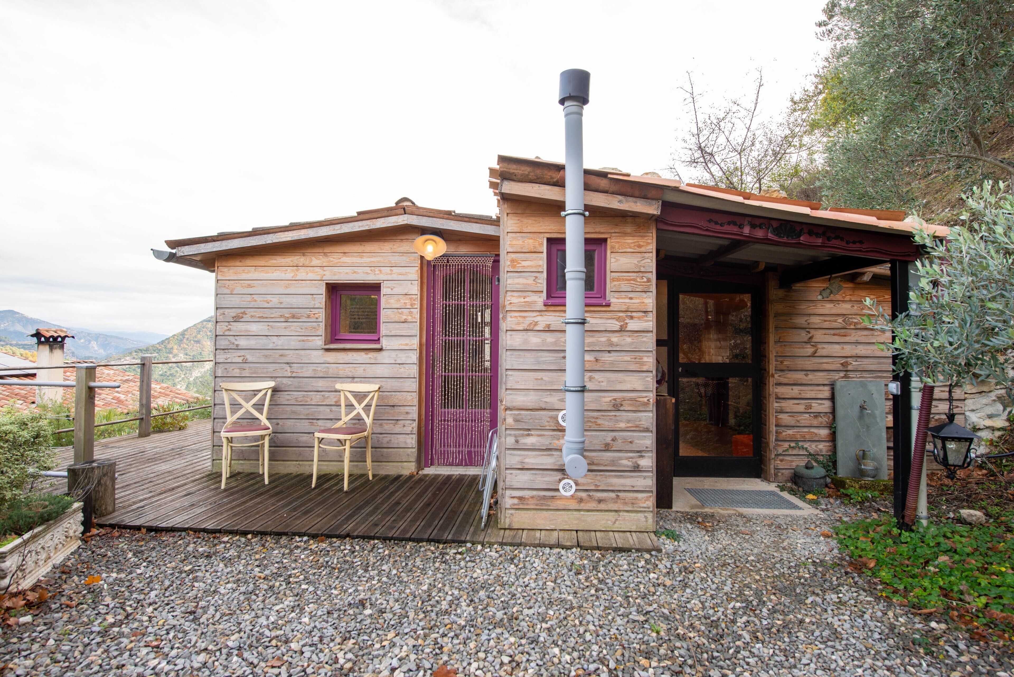 A rustic wooden cabin with a purple door, two chairs on a wooden deck, and a view of the mountains in the background.