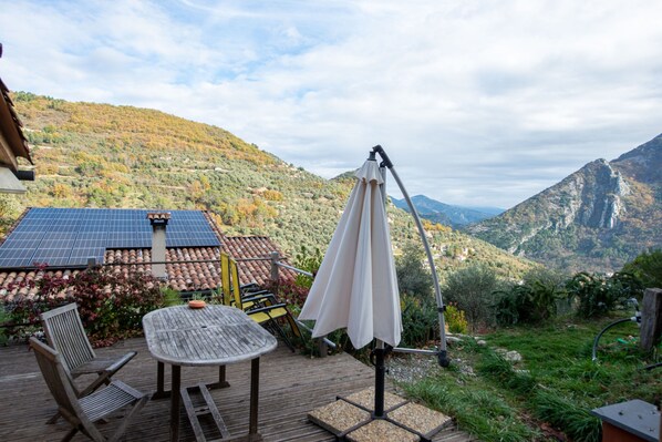A deck with a table and chairs, solar panels, and a view of a mountainous landscape.