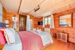 Ein Schlafzimmer einer Holzhütte mit Bett, Fernseher, Fenster und Spiegel.