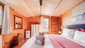 Een slaapkamer in een houten hut met een bed, een raam, een schilderij en een kleine kitchenette.