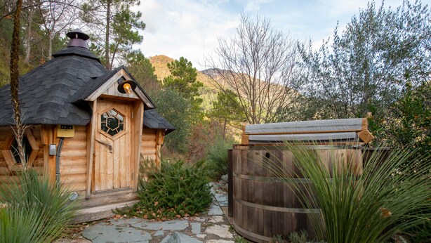 Een houten chalet met een zeshoekig raam, een pad van stenen en een houten vat.