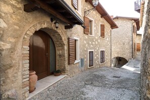 Une ruelle étroite pavée de pierres, bordée de bâtiments en pierre, avec une porte en arc de cercle et un pot de fleurs.
