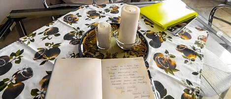 Un tavolo con tovaglia floreale, un libro, due candele e un portatile.