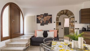 Una sala de estar con un sofá, una mesa de vidrio, una obra de arte con un mapa del mundo y un arco de piedra.