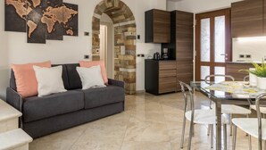 Una sala moderna con sofá, una mesa de comedor con sillas, un área de cocina con armarios y un arco de piedra.