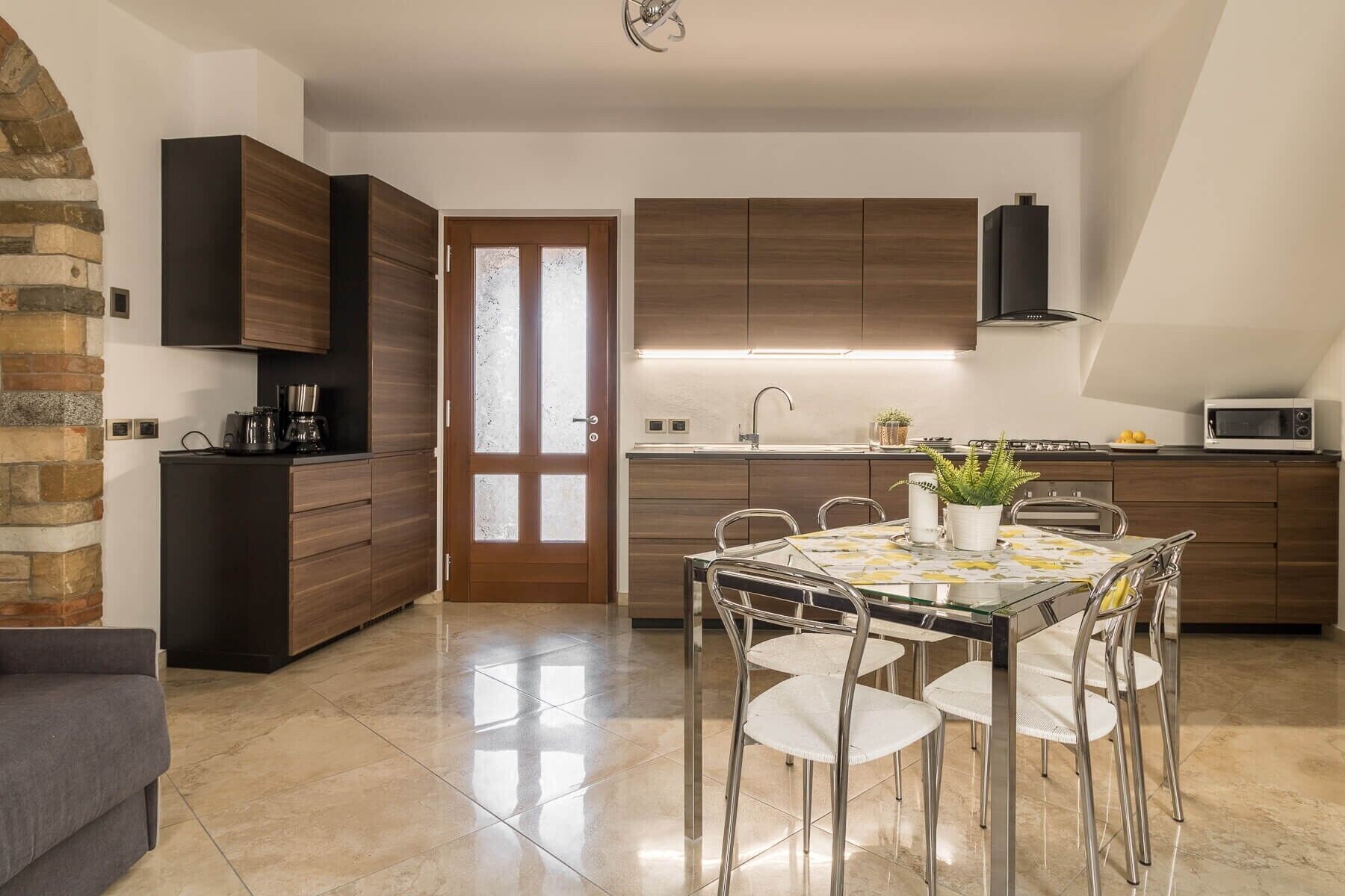 Una cocina moderna con comedor, que presenta una pared de piedra, armarios de madera y suelo de baldosas.