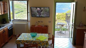 A kitchen with a dining table, chairs, a TV, and a view of greenery and water. - Apartment 'El Pià' with Lake View and Private Garden (tignale)