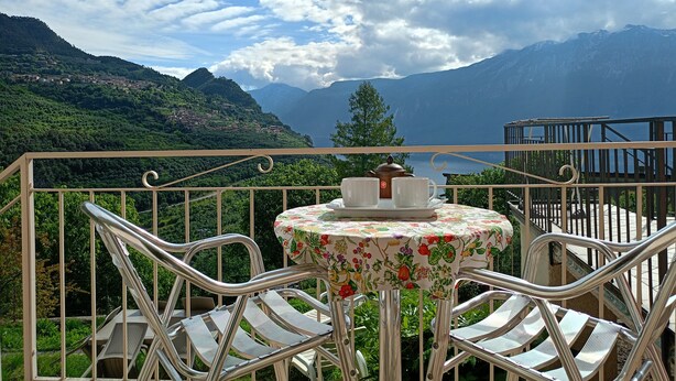 A balcony with a table and chairs, overlooking a mountainous landscape. - Apartment 'El Pià' with Lake View and Private Garden (tignale)