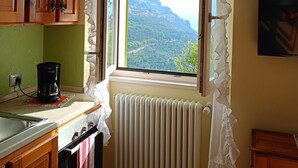 A kitchen with wooden cabinets, a coffee maker, a window with a view of a mountainous landscape, and a radiator. - Apartment 'El Pià' with Lake View and Private Garden (tignale)
